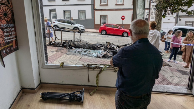 Una persona observa el cristal roto de la asociación Cántigas da Terra tras el incendio en unos contenedores en La Coruña