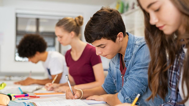 Group of college students studying in classroom writing notes during lesson. Focused guy and girls studying in college library sitting at desk. Group of multiethnic university students doing research sitting in a row.