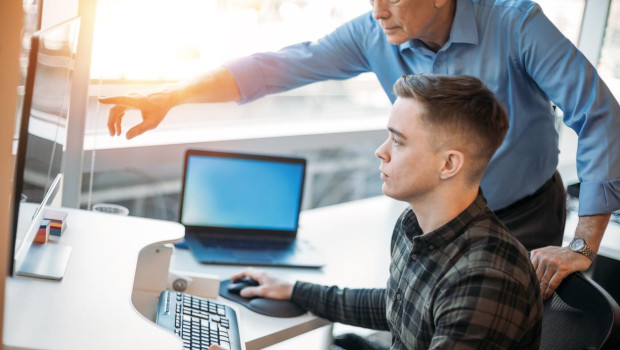 Colleague mentoring younger associate in business office while pointing at data on computer monitor