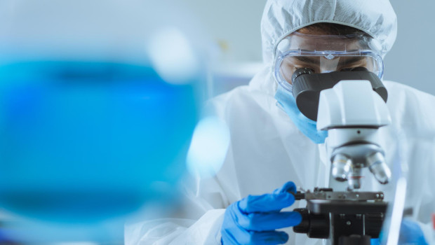 Imagen de archivo de un científico mirando un microscopio vestido con un EPI