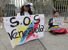 Una pareja de ciudadanos venezolanos sostiene carteles afuera de la embajada de Venezuela este martes, en el barrio de Providencia en Santiago (Chile)