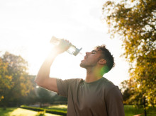 Un joven atleta se hidrata con agua fresca de una botella después de hacer ejercicio en un parque al atardecer durante el verano