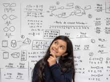 Portrait of a thoughtful schoolgirl thinking about a mathematical problem at the school and leaning against a whiteboard