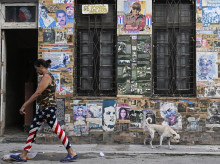 Una mujer con leggings con la bandera de Estados Unidos y un perro pasan junto a una casa