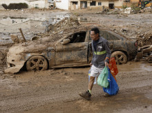 Un hombre con productos de primera necesidad pasa ante una zona anegada de barro en Paiporta