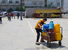 Un joven palestino lucha por transportar un carro lleno de contenedores de agua en un punto de distribución del campo de refugiados de Nuseirat