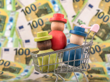 Personas de madera en un carrito de la compra, sobre un fondo con dinero