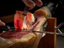 Close up of cutter gourmet hands slicing acorn fed iberian ham. Typical and traditional spanish delicatessen pork food.