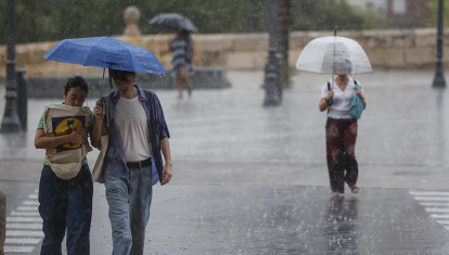 Imagen de archivo de personas con paraguas y ropa veraniega paseando bajo la lluvia en Valencia