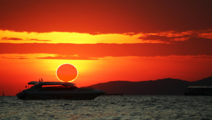 Fenómeno increíble de eclipse de sol parcial sobre barco de silueta en el mar y el cielo de la puesta de so