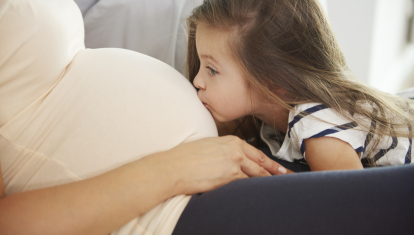 Hermana mayor dando un beso en la tripa su mamá