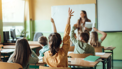 Estudiantes levantando la mano mientras el maestro les hace preguntas en el aula