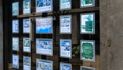 Barcelona, Spain-February 1, 2025. Glass window of a real estate agency displaying illuminated property listings for sale and rent, reflecting the urban environment outside.