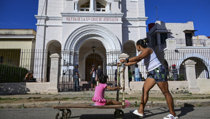 Una mujer empuja un carrito con su hija frente a la Iglesia de la Santa Cruz de Jerusalén en La Habana