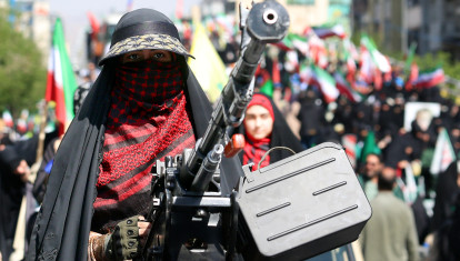 Una mujer iraní se encuentra junto a una ametralladora pesada montada en la parte trasera de un vehículo