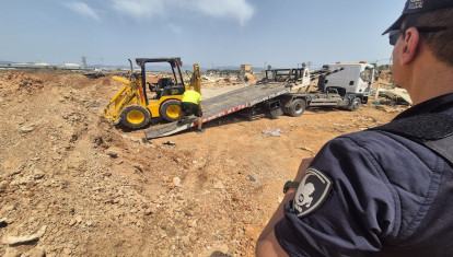 Un agente de la Policía Local de Palma observa la retirada de una retroexcavadora en unos terrenos públicos