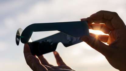 Person holding paper solar eclipse glasses, blocking the sun's direct rays for safe viewing during an astronomical event