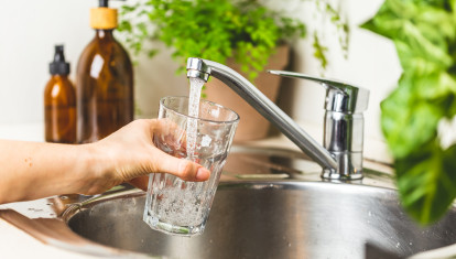 Female hand holding a glass and pouring it with tap water in the kitchen at home. Stay hydrated and filtering water concept. World water day