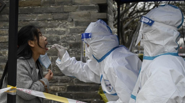 Un sanitario toma una muestra de saliva a una joven en Pekín