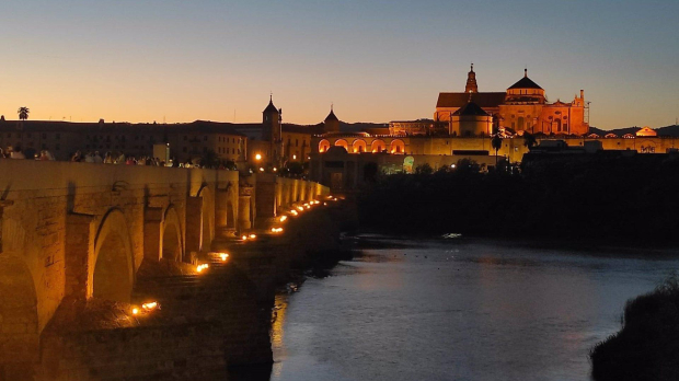 Turistas cruzan el Guadalquivir por el Puente Romano de Córdoba, con la Puerta del Puente y la Mezquita-Catedral al fondo