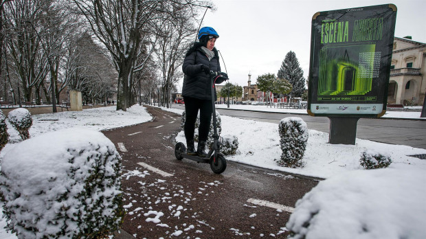 Una mujer conduce un patinete eléctrico por una calle cubierta de nieve