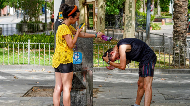 Una joven le hace una foto a un joven mientras le está refrescando la cabeza en Sevilla