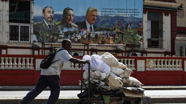 Un hombre empuja una carretilla frente a un mural de los líderes de la dictadura cubana
