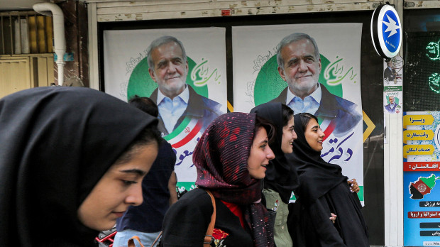 Las mujeres pasan junto a carteles electorales del candidato presidencial reformista iraní Massoud Pezeshkian en una calle de Teherán
