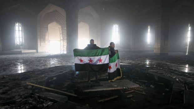 Los combatientes rebeldes sostienen la bandera de la revolución en la tumba quemada del difunto presidente sirio Hafez al-Assad