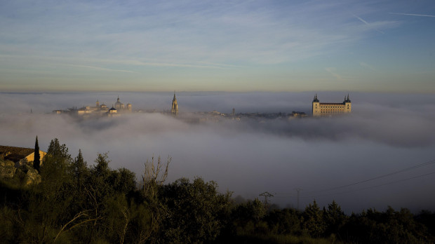 La niebla que cubre por completo el casco histórico de Toledo, a primera hora de la mañana, empieza a dejar ver el campanario de la catedral primada y el Alcázar de la ciudad. EFE/Ismael Herrero