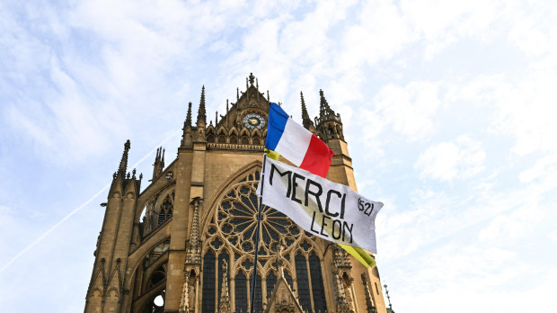 Una persona agita una bandera nacional francesa y una pancarta en la que se lee en francés «Gracias, León» mientras espera frente a la catedral de Saint-Étienne, en Metz