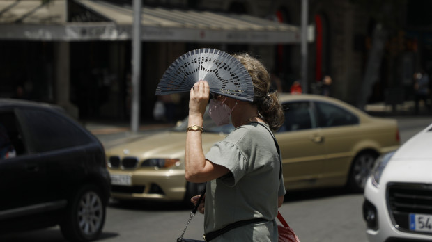 A woman crosses a street and covers herself with a fan in Palma de Mallorca during a heat wave.