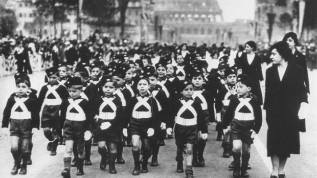 While it may be quite a spell before these youngsters see any real action, there's not doubt about their being real Italian "soldiers" known by the ferocious names of "Sons of the Wolf." They range in years from 6 to 8, and are seen in Rome, on June 8, 1935, when they passed in review before Mussolini, who has ordered military training for all males from 6 years to 33. (AP Photo)