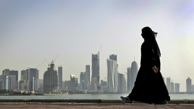 FILE- In this May 14, 2010 file photo, a Qatari woman walks in front of the city skyline in Doha, Qatar. A worker on a Qatar World Cup stadium site has died in the first work-related fatality to be announced by organizers of the 2022 soccer tournament which has been dogged by concerns about labor conditions. Qatar has previously reported three deaths at stadium construction sites but said they were not “work-related.” (AP Photo/Kamran Jebreili, File)