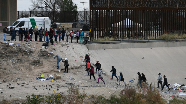 Inmigrantes caminan a lo largo del lado estadounidense del río Bravo debajo del muro fronterizo para entregarse a los agentes de la Patrulla Fronteriza de EE.UU. en El Paso, Texas