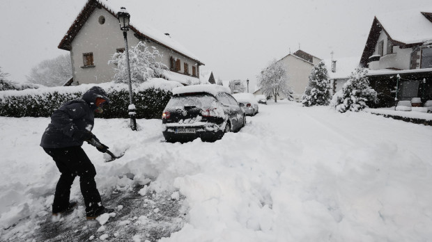 Una persona intenta limpiar de nieve para poder sacar su vehículo de una calle de la localidad de Espinal donde una intensa nevada caída durante la jornada de este lunes cubre completamente la carretera