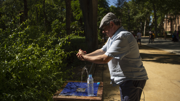 Un hombre se refresca con el agua de una fuente en Sevilla