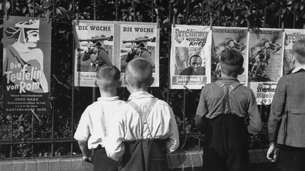 Niños alemanes observan el periódico antisemita Der Stürmer y otros carteles de propaganda nazi