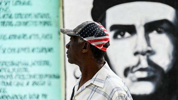 Un hombre con una gorra de EE.UU. camina junto a un letrero con la imagen del Che en La Habana