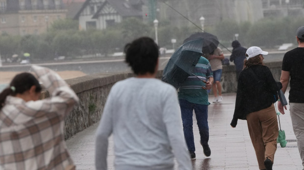 Varias personas caminan bajo la lluvia en la playa de Ondarreta, en San Sebastián