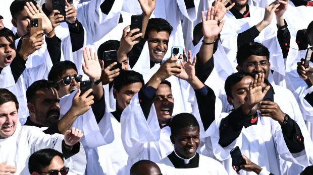 Los sacerdotes saludan mientras el Papa León XIV saluda a la multitud desde el papamóvil antes de la Santa Misa de inicio de su pontificado
