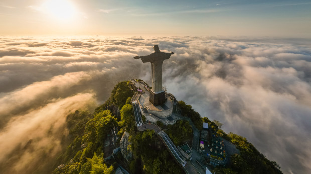 Rio de Janeiro, Brazil - April 11, 2024: Dramatic view of Christ the Redeemer statue on top of the Corcovado mountain above clouds during sunrise.