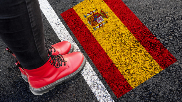 a woman with a boots standing on asphalt next to flag of Spain and border