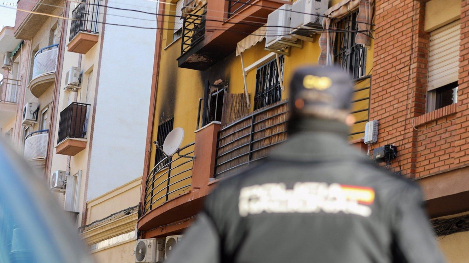 Un agente de la Policía Nacional mira en dirección a la vivienda que ha sufrido el incendio en Huelva