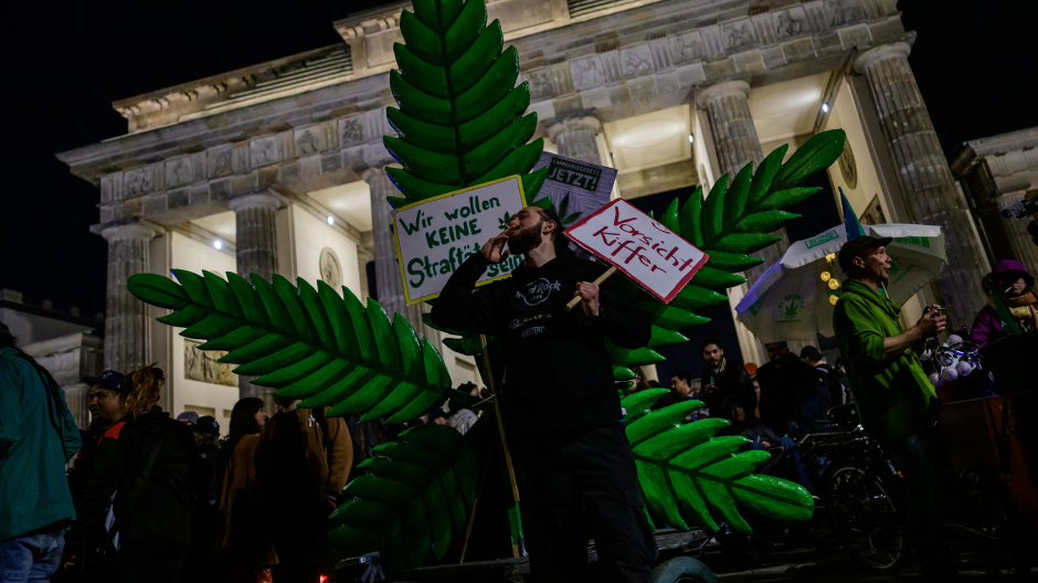 Un fumador de marihuana fuma un porro frente a una planta gigante de marihuana simulada durante una manifestación frente a la Puerta de Brandenburgo