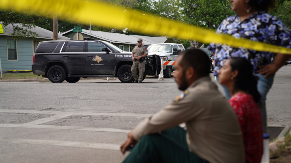 La gente se sienta en la acera afuera de la Escuela Primaria Robb mientras la policía estatal protege el área en Uvalde, Texas