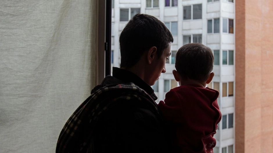 Un padre mirando por la ventana con su hijo en brazos