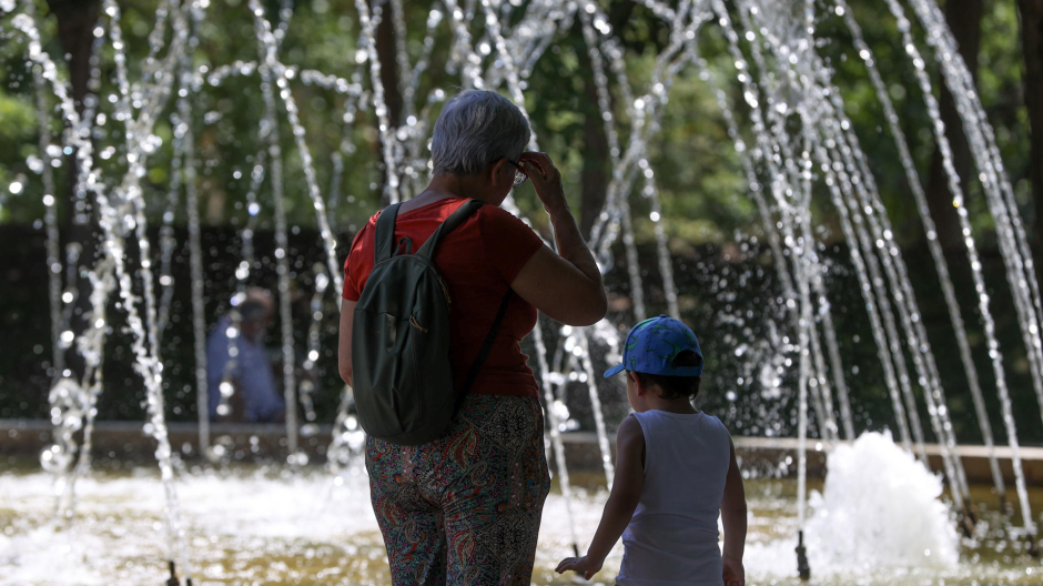 Niños y adultos se refrescan a la sombra, junto a las fuentes públicas del parque del Retiro