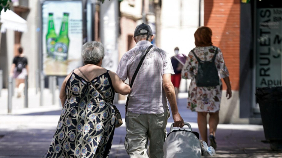Una pareja de ancianos camina por la calle con un carro de compra.