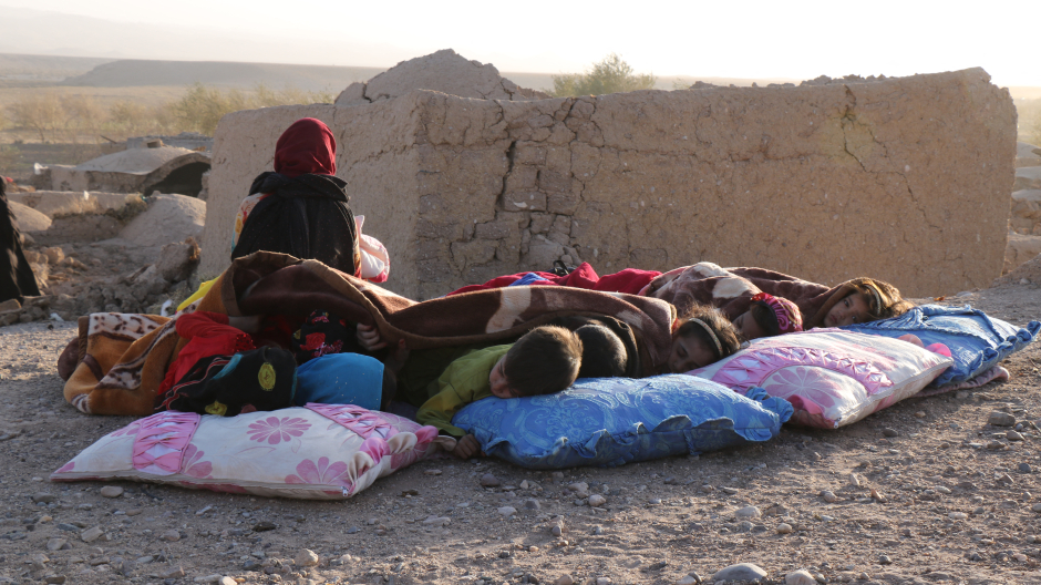 Los niños afganos descansan bajo una manta junto a las casas dañadas tras el terremoto en la aldea de Sarbuland